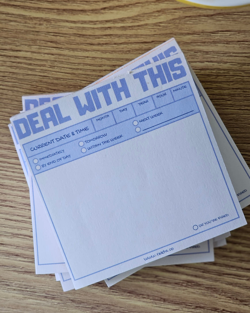 A stack of white notepad sheets with blue printed text and fields, placed on a wooden tabletop next to a cup of coffee.