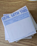 A stack of white notepad sheets with blue printed text and fields, placed on a wooden tabletop next to a cup of coffee.