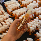 A hand holds a small amber spray bottle with a clear trigger sprayer and orange loop, branded 'RingCenter', in front of a table covered with many identical bottles.